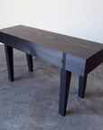 A small scaled handcrafted bench with a wooden seat and legs, displayed against a simple background.