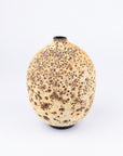 A textured ceramic vase with a rounded, bulbous shape, featuring a speckled pattern of dark brown spots on a warm beige and cream glaze, set against a plain white background.