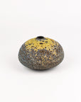 A small organic-shaped ceramic vase with a textured, speckled finish, featuring a yellow glazed top half and a dark speckled bottom half, set against a plain white background.