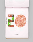 A single-page calendar page from a hanging wall calendar, showing the day Friday with a decorative orange dot pattern and a green-and-brown block design, photographed against a plain light gray background.