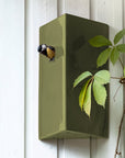 Green birdhouse on a white wooden wall with a bird perched on top