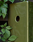 Green ceramic bird house entry detail on a dark background with green leaves.