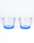 Two small textured blue glass tumblers with a hammered pattern, shown side by side on a clean white background.