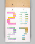 A white rectangular card or print with colorful geometric numbers and symbols arranged to spell '2027', attached to a brown kraft paper backing with two small black dots near the top, shown against a light gray background.