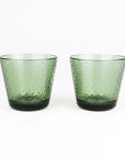 A pair of textured green glass tumblers with a hammered pattern and dark green bases, set against a plain white background.