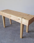 A small scaled handcrafted bench with a wooden seat and legs, displayed against a simple background.