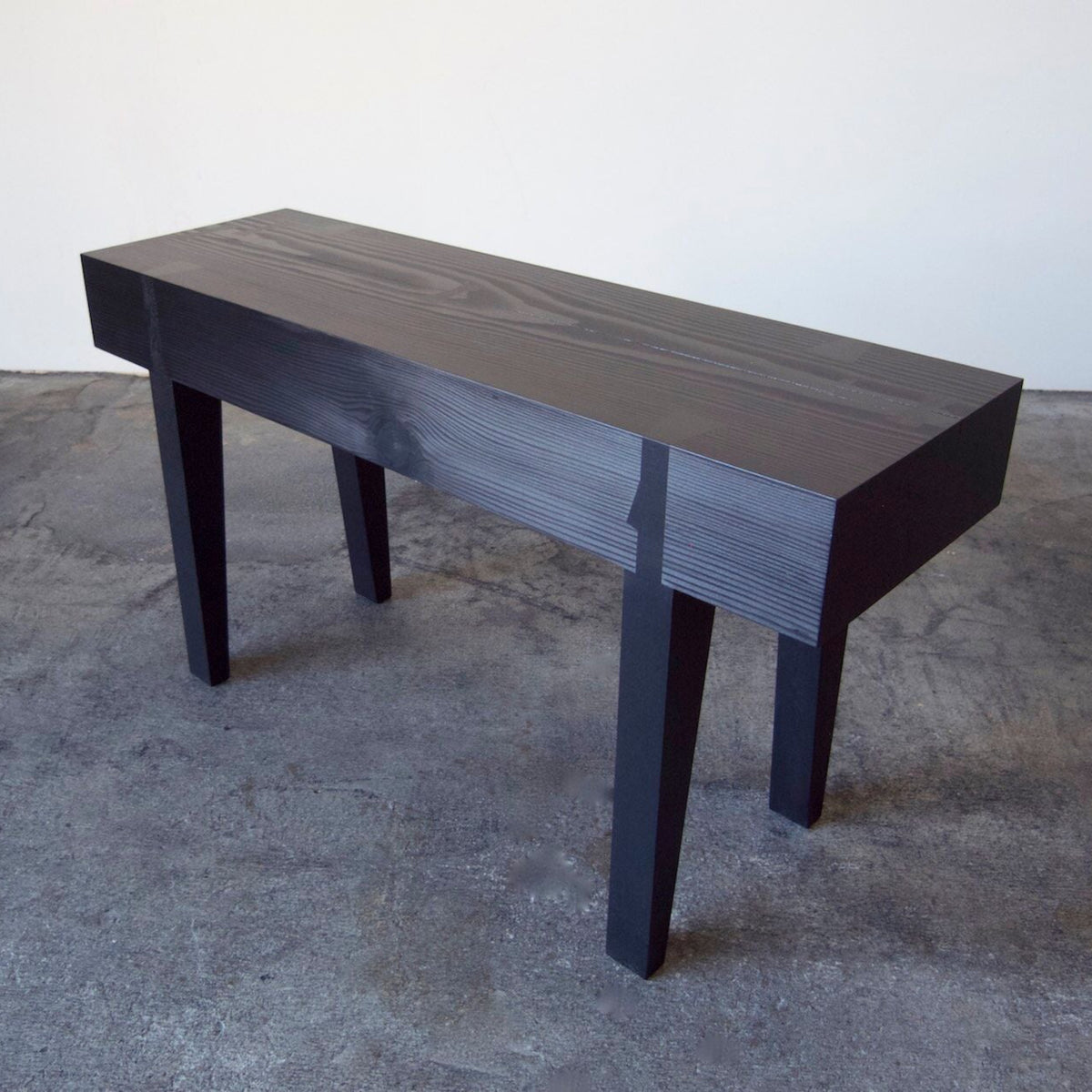 A small scaled handcrafted bench with a wooden seat and legs, displayed against a simple background.