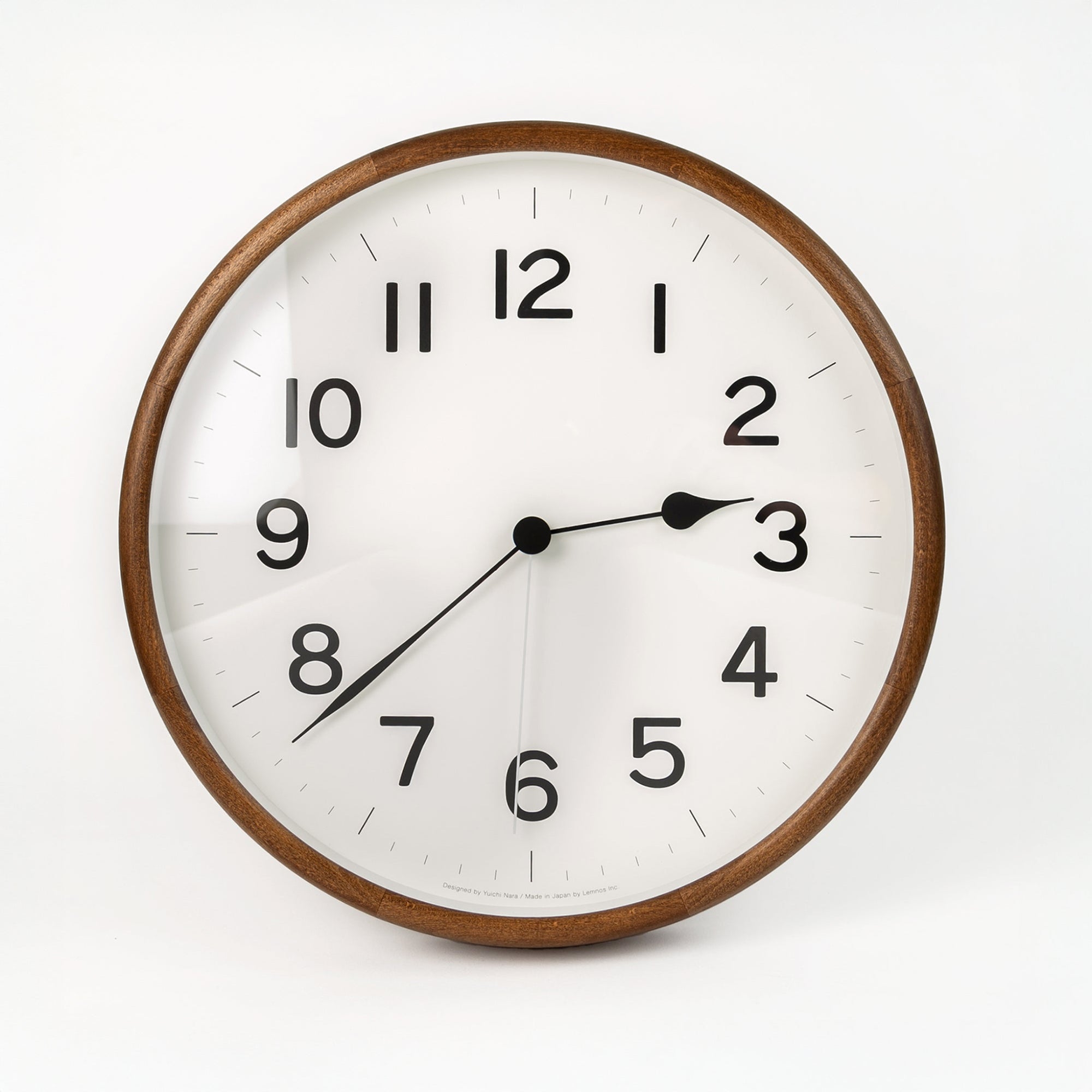 A round wall clock with a dark stained wooden frame and a glass face. The clock has black hands and numbers, with a white background.