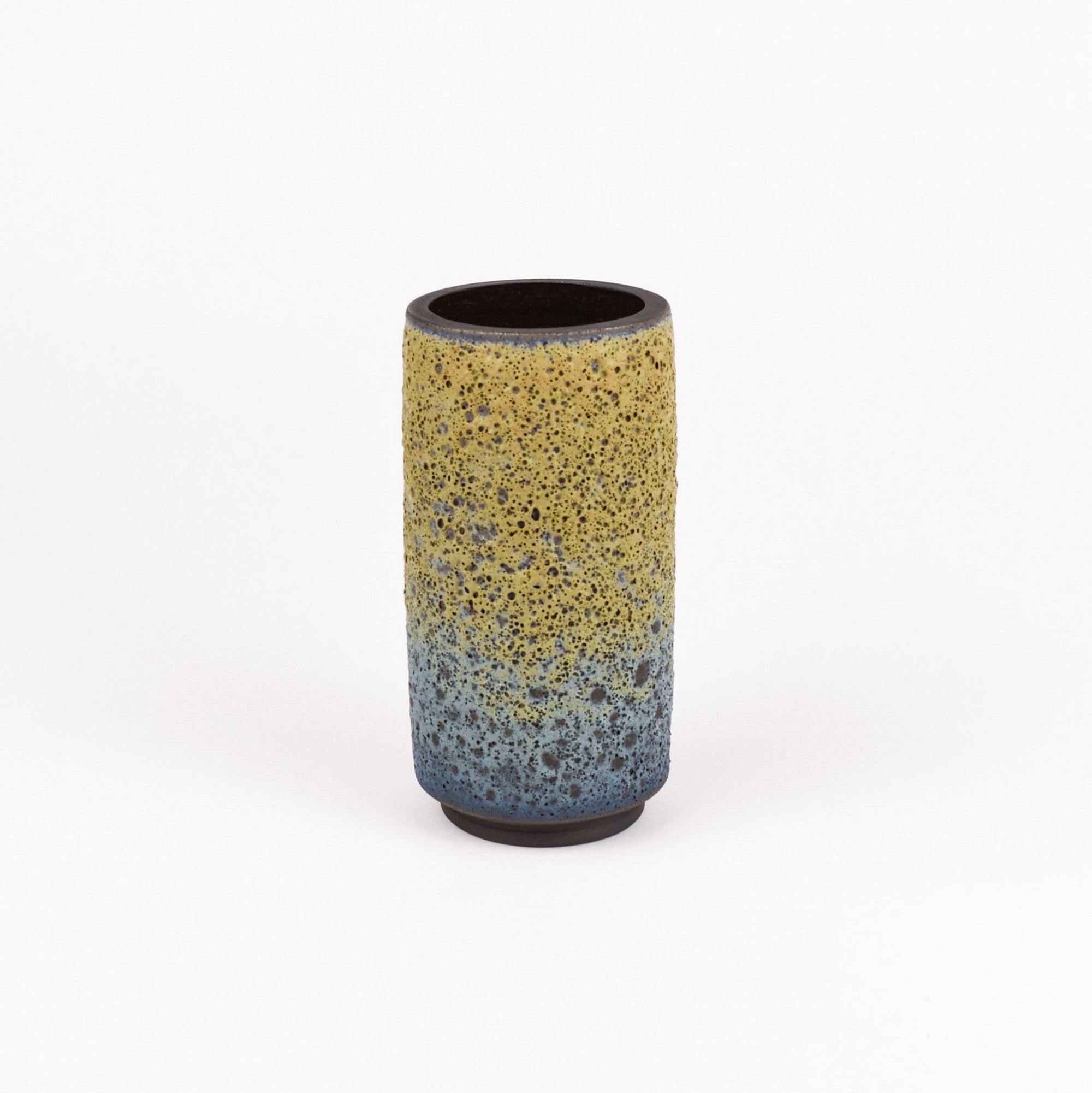 A cylindrical ceramic vase with a textured, speckled glaze featuring a yellow-to-blue gradient and dark brown base, set against a plain white background.