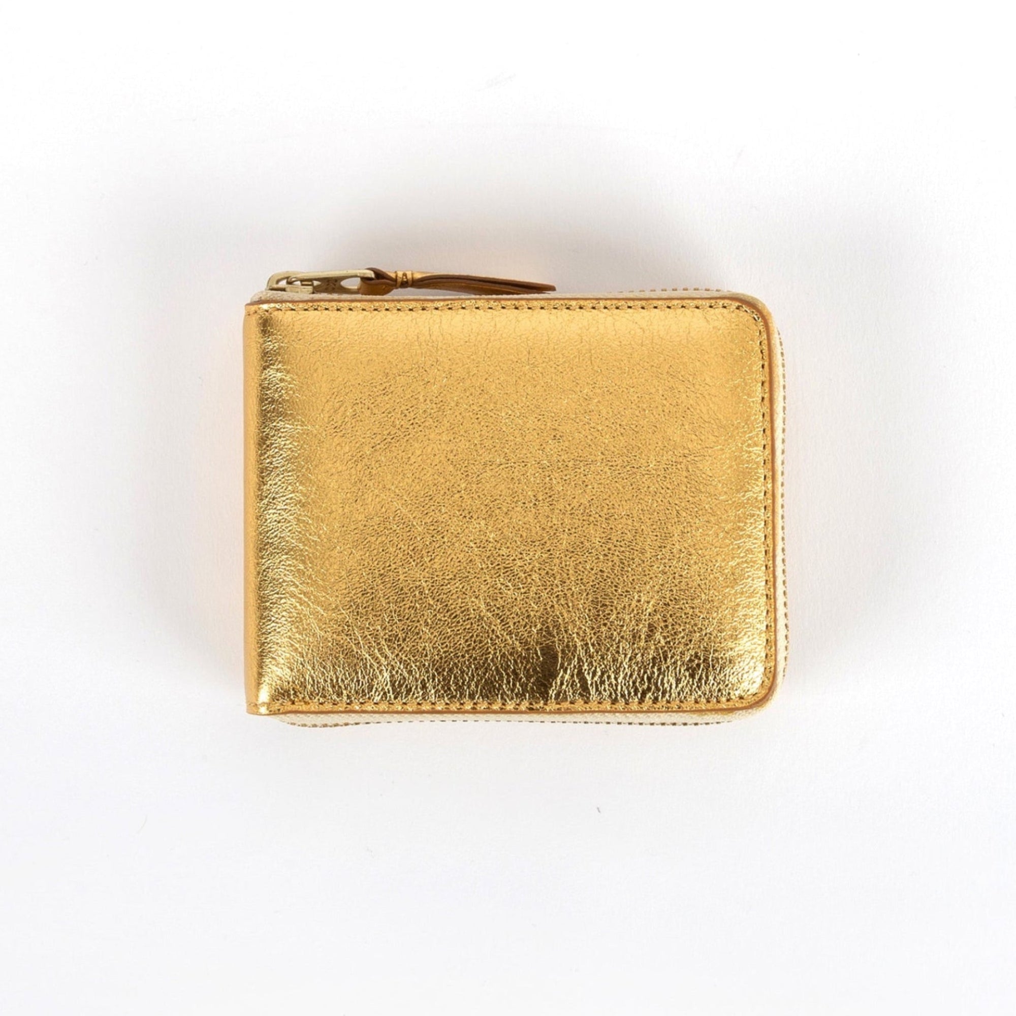 A gold-colored, metallic Comme des Garcons wallet with a zipper closure.
