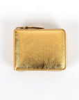 A gold-colored, metallic Comme des Garcons wallet with a zipper closure.