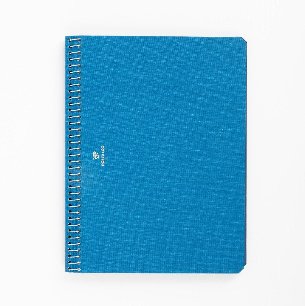 A blue A5 sized notebook with a stylized carrier pigeon logo on the cover, binding visible on the side.