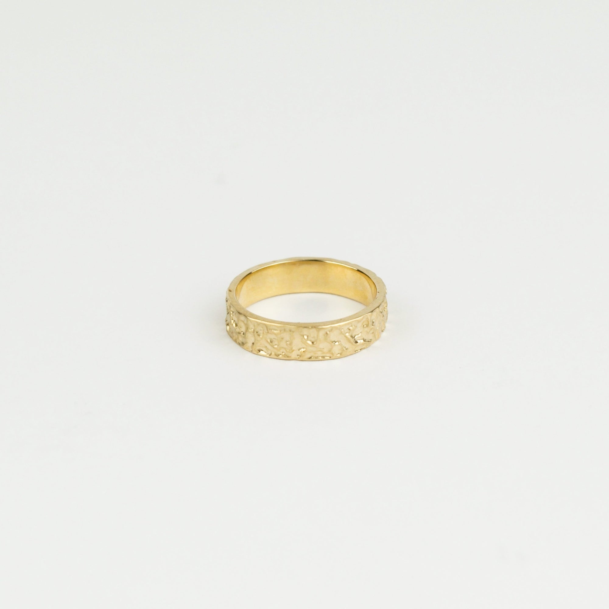 Gold ring with textured design on a light gray background