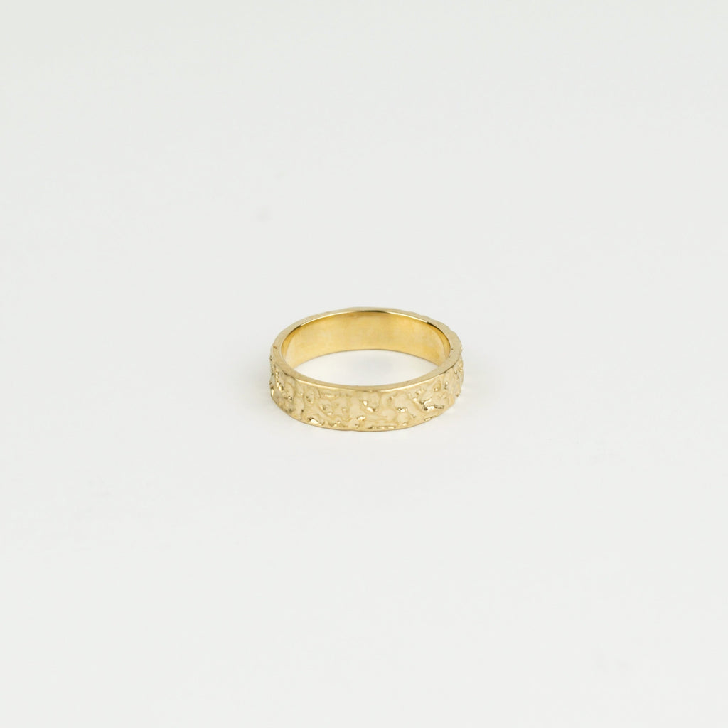 Gold ring with textured design on a light gray background