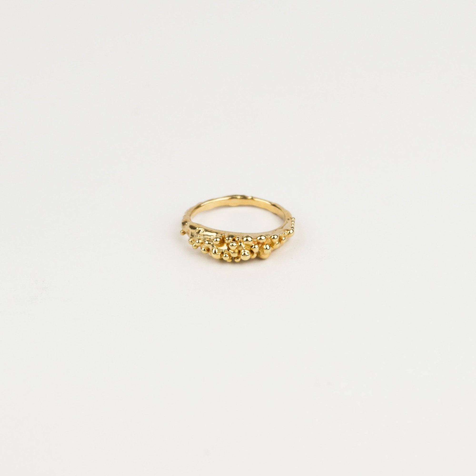 Gold ring with small beads on a light beige background