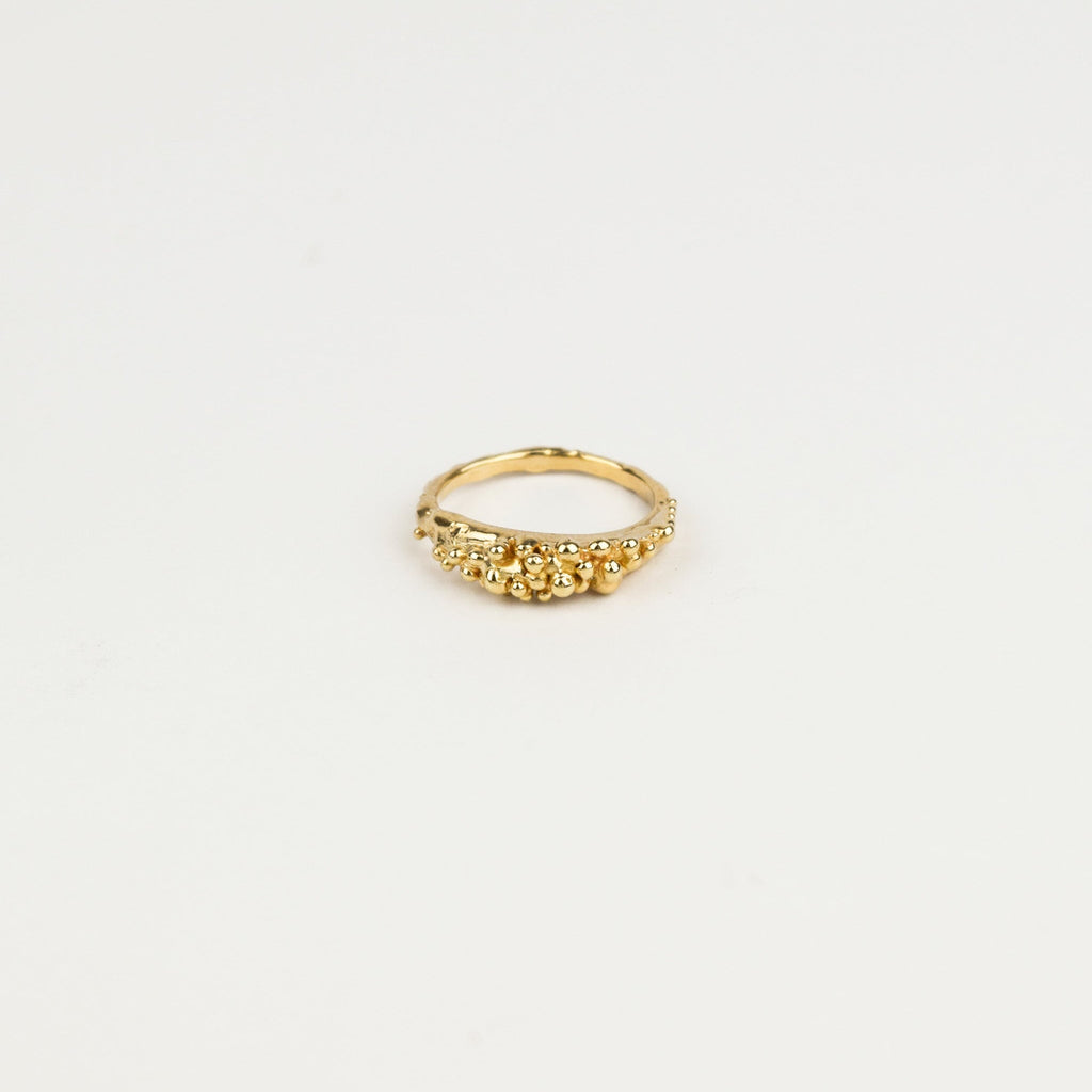 Gold ring with small beads on a light beige background