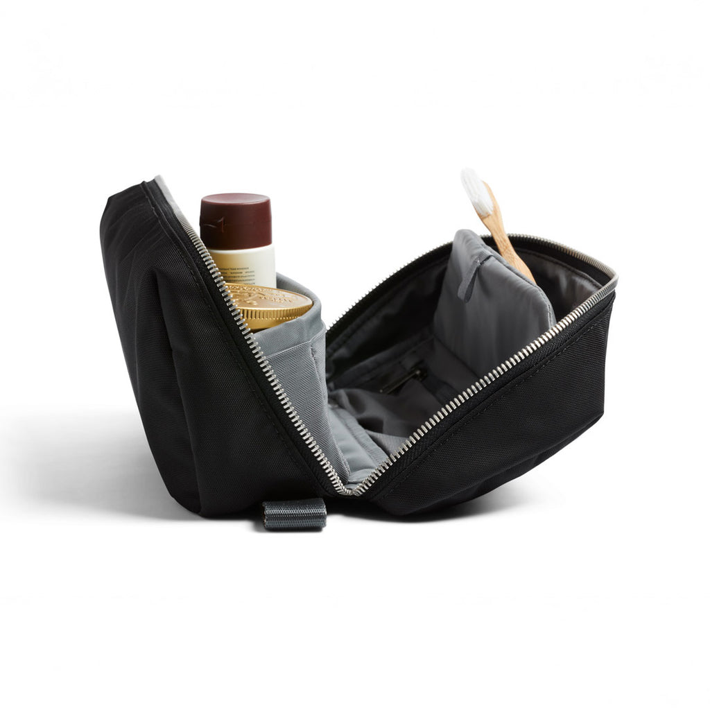 Black toiletry bag with gray interior containing travel items on a white background