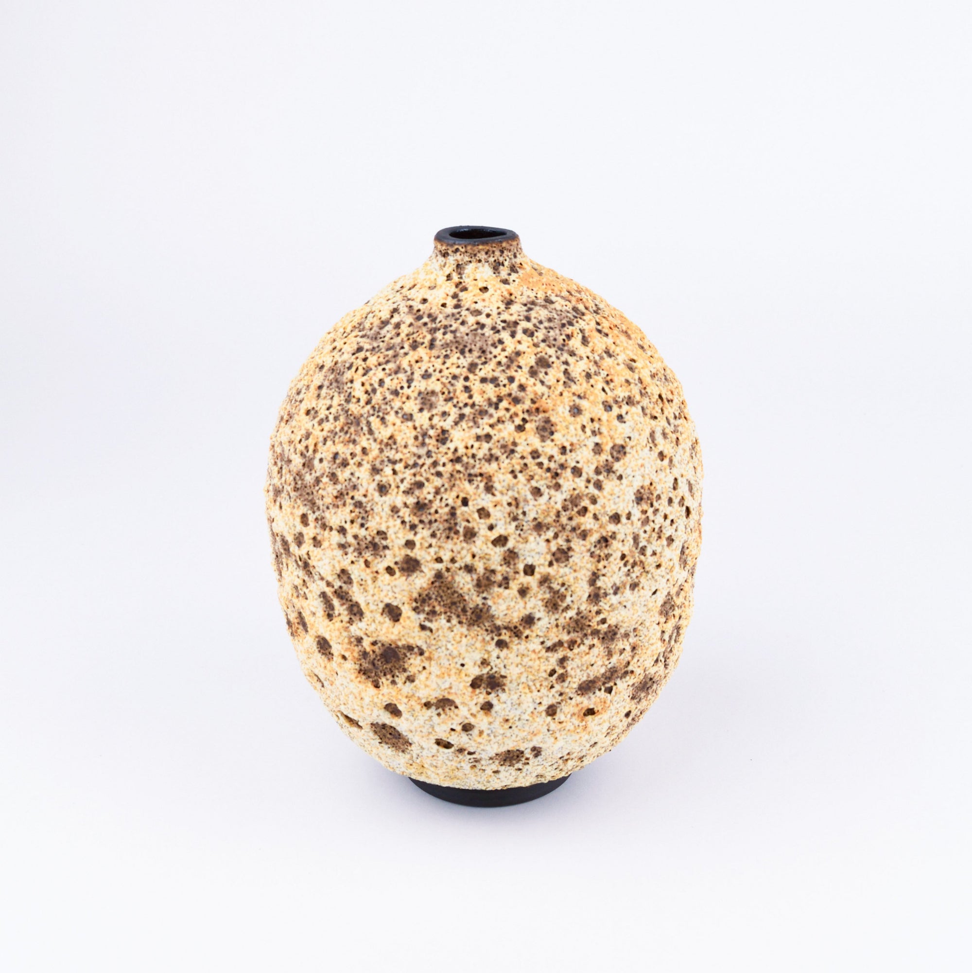 A textured ceramic vase with a rounded, bulbous shape, featuring a speckled pattern of dark brown spots on a warm beige and cream glaze, set against a plain white background.
