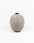 A small ceramic vase with a rounded, bulbous shape and a speckled glaze in warm beige and gray tones, set against a plain white background.