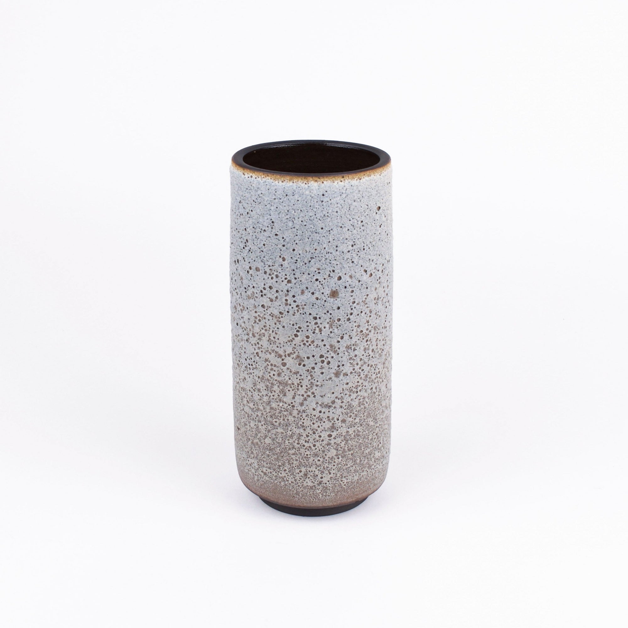 A tall, cylindrical ceramic vase with a speckled glaze that transitions from light gray at the top to a warm brown at the base, set against a plain white background.