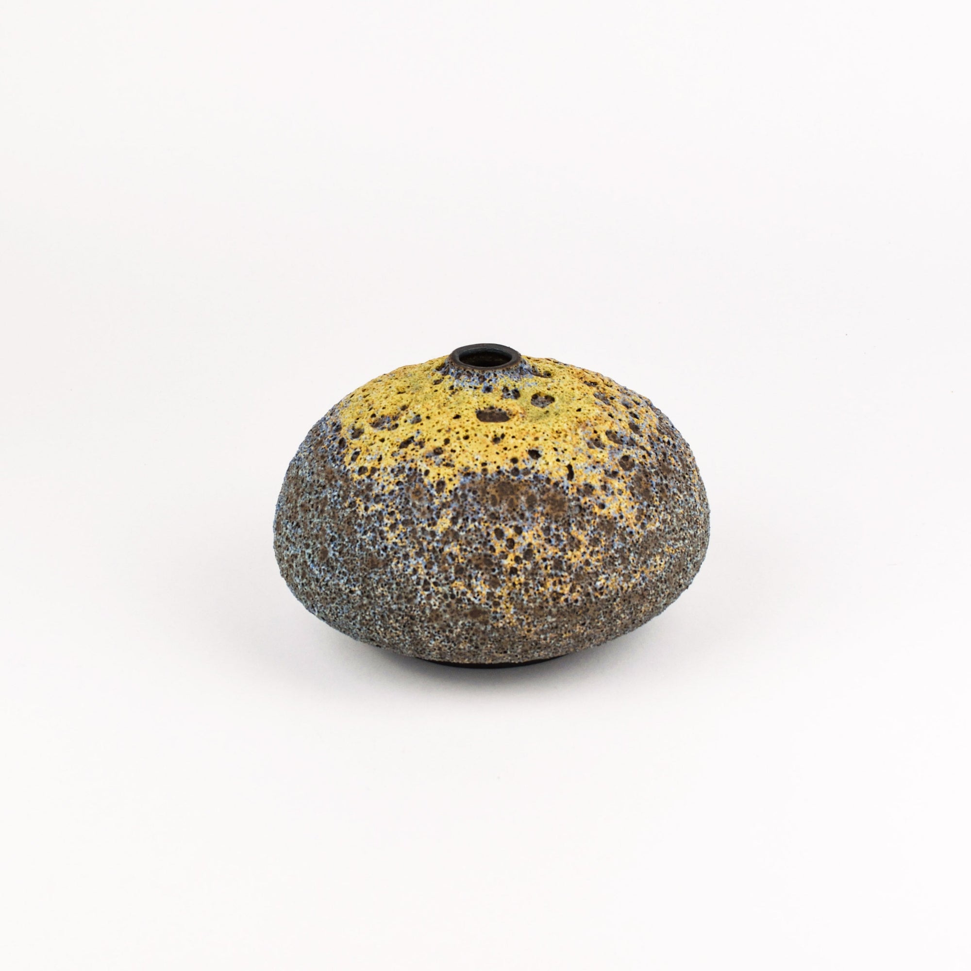 A small organic-shaped ceramic vase with a textured, speckled finish, featuring a yellow glazed top half and a dark speckled bottom half, set against a plain white background.