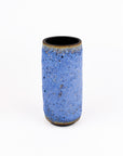 A small cylindrical ceramic vase with a textured blue glaze and a dark, unglazed black interior, set against a plain white background.