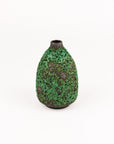 A small textured ceramic vase with a rounded body, narrow neck, and dark base, decorated with a mottled green and brown speckled glaze, set against a plain white background.