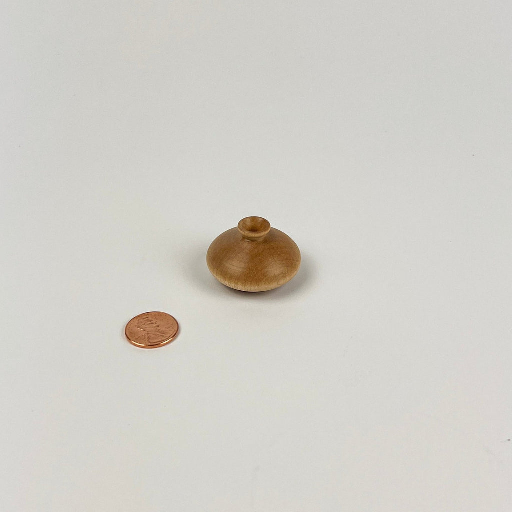 Small wooden vase next to a penny on a white background