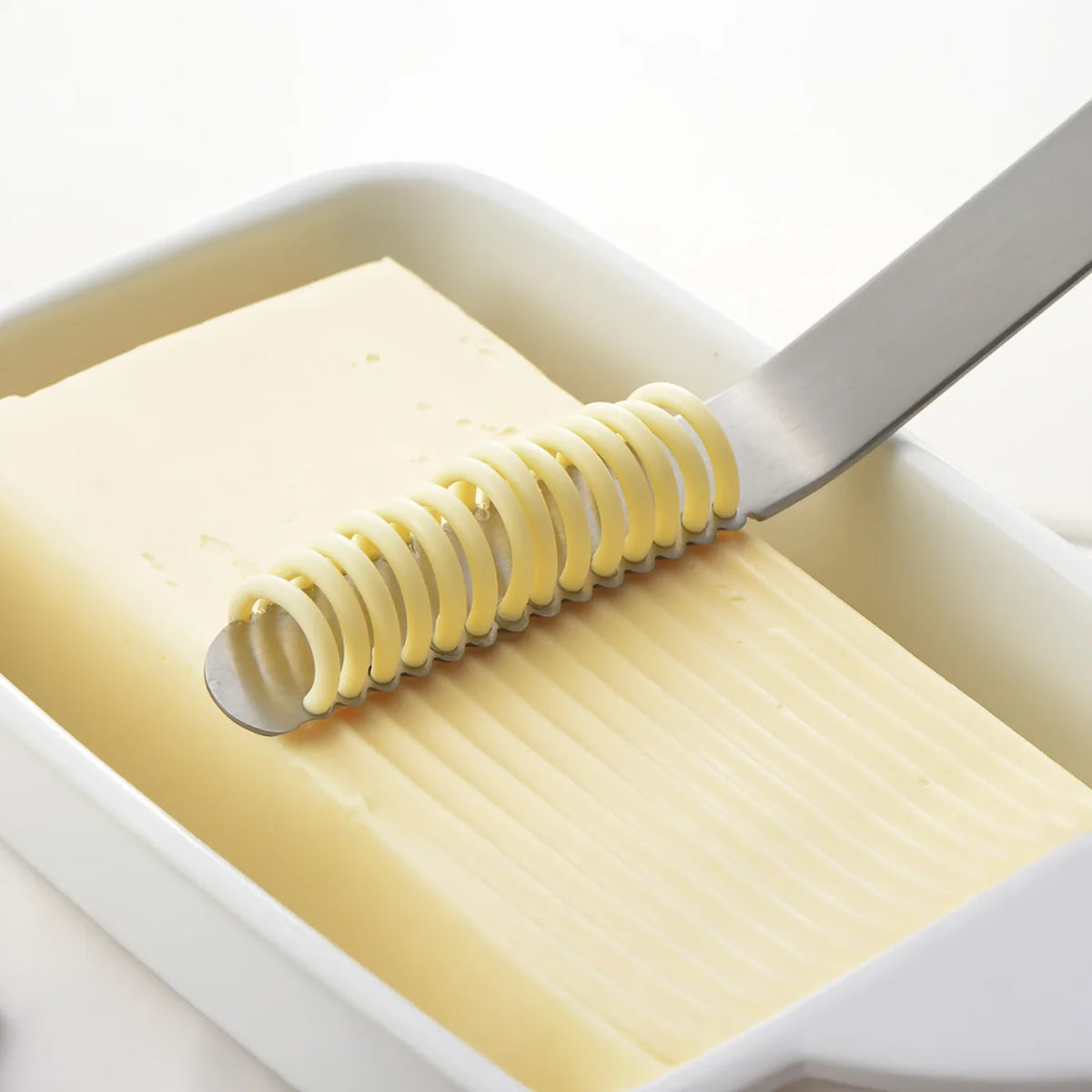 Butter being sliced with a butter knife on a white background