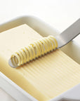 Butter being sliced with a butter knife on a white background