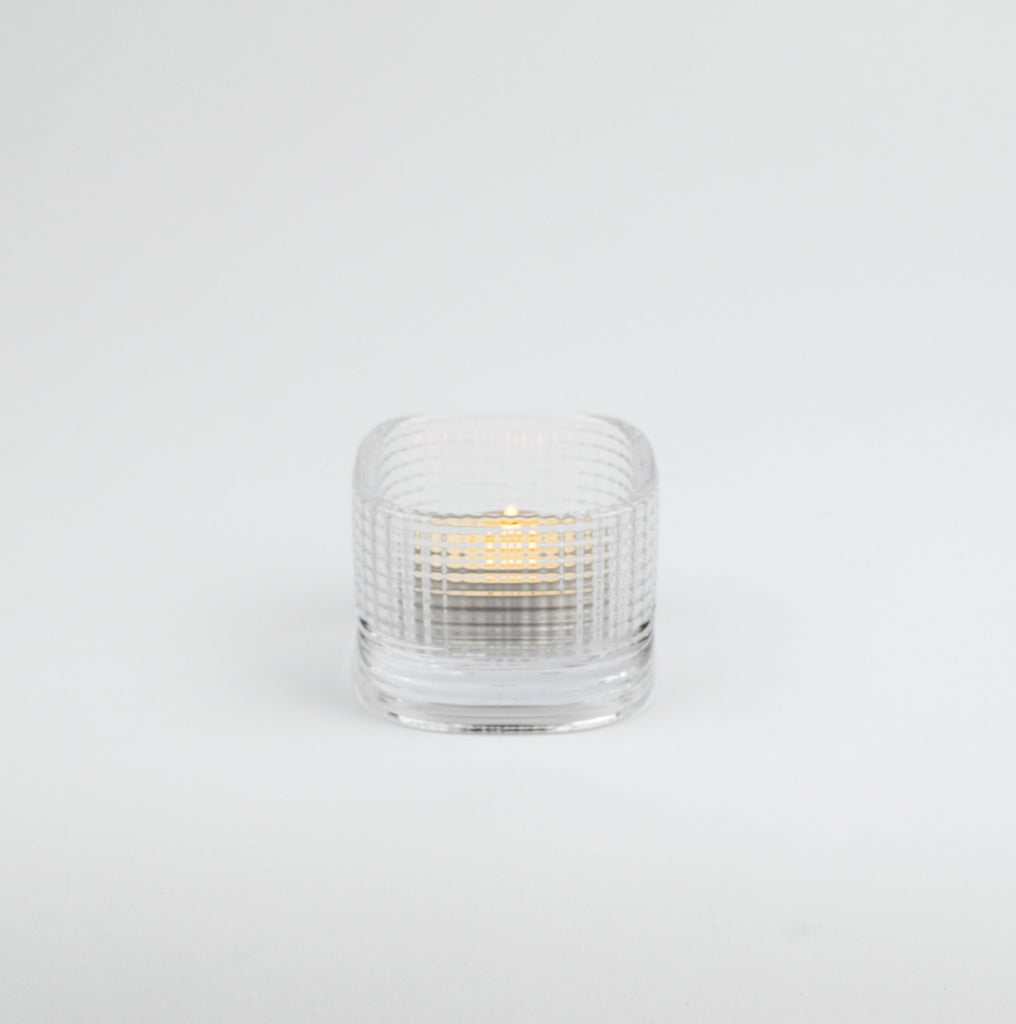 Clear glass candle holder with a lit candle on a white background