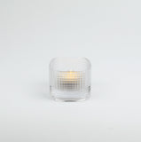 Clear glass candle holder with a lit candle on a white background