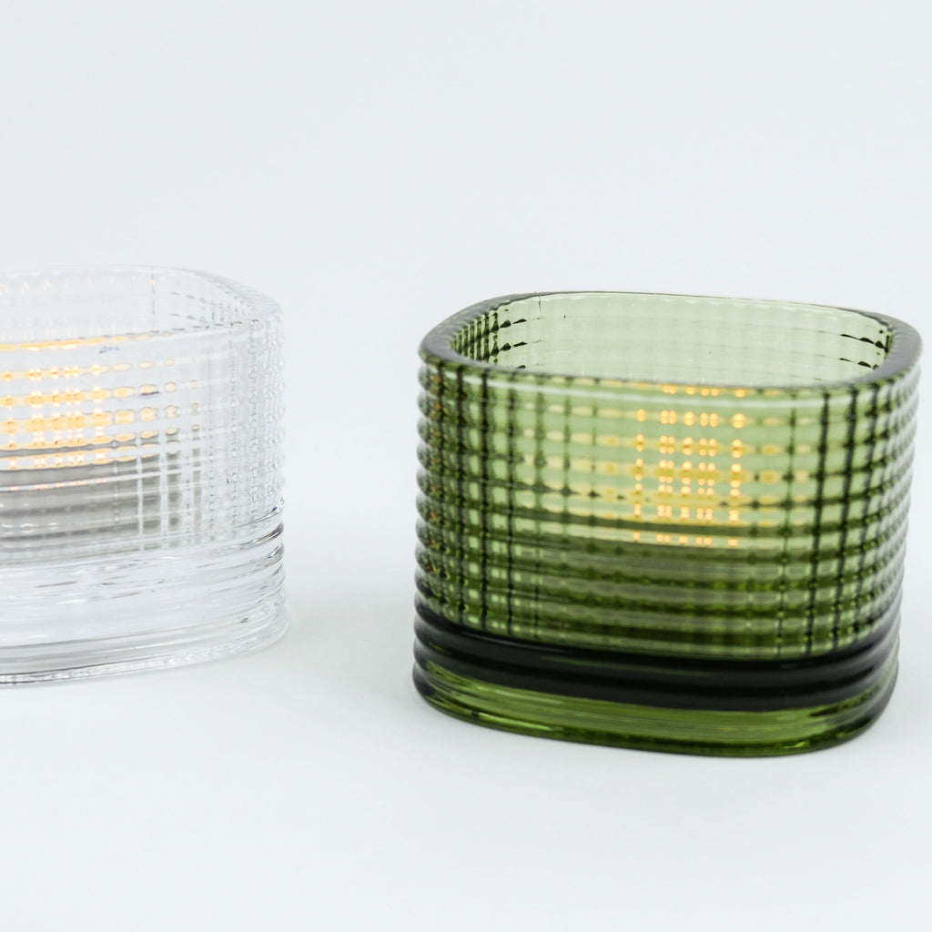 Green textured glass candle holder with a lit candle inside on a white background