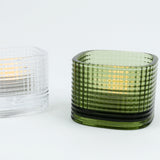 Green textured glass candle holder with a lit candle inside on a white background