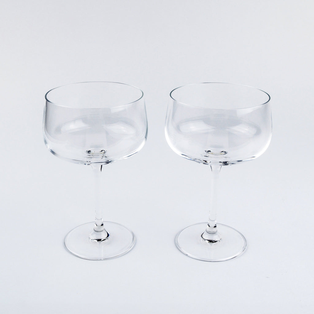 Two clear glass coupe glasses on a light gray background