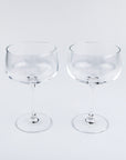 Two clear glass coupe glasses on a light gray background
