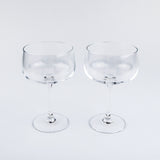 Two clear glass coupe glasses on a light gray background