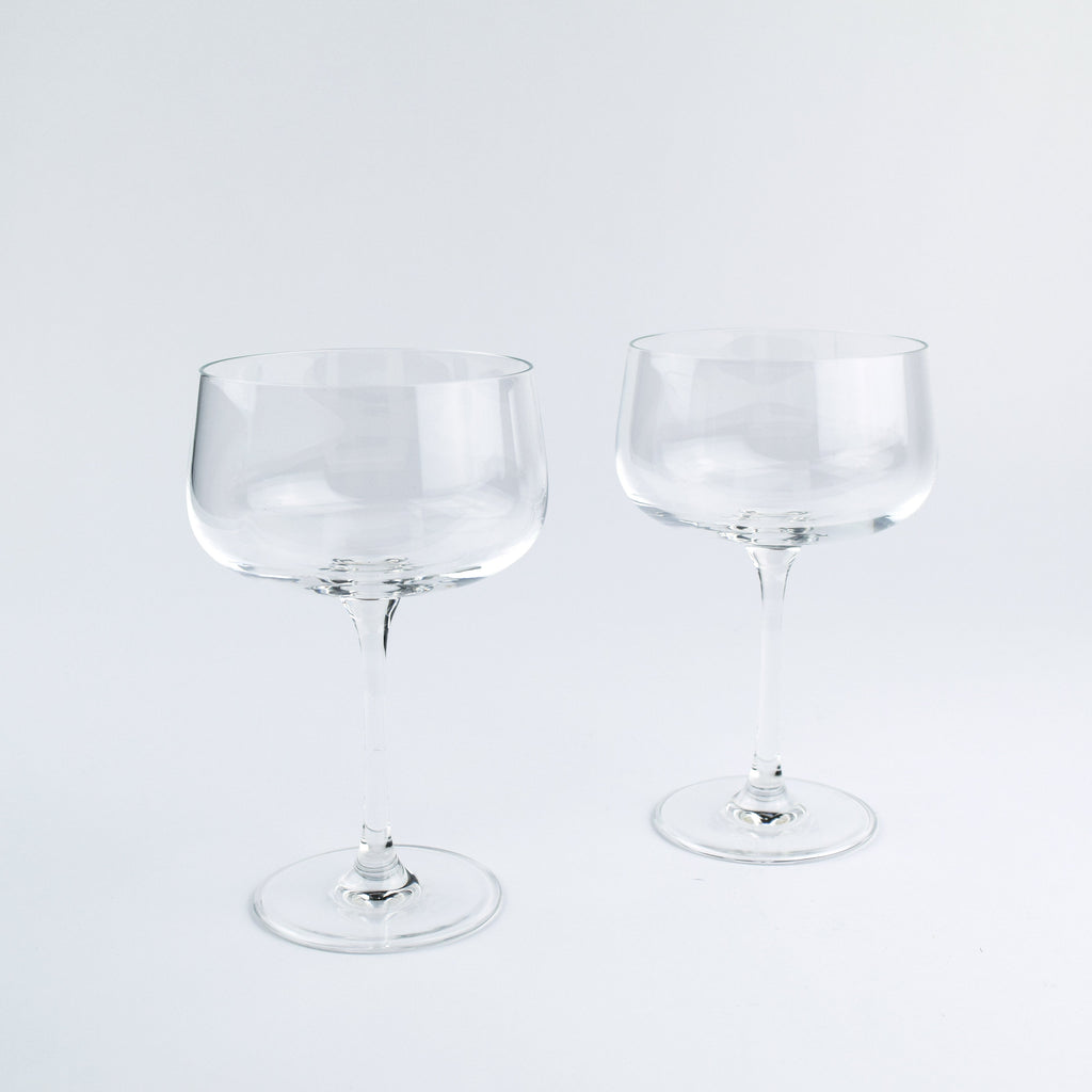 Two clear glass coupe glasses on a light gray background