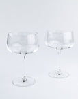 Two clear glass coupe glasses on a light gray background