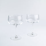 Two clear glass coupe glasses on a light gray background