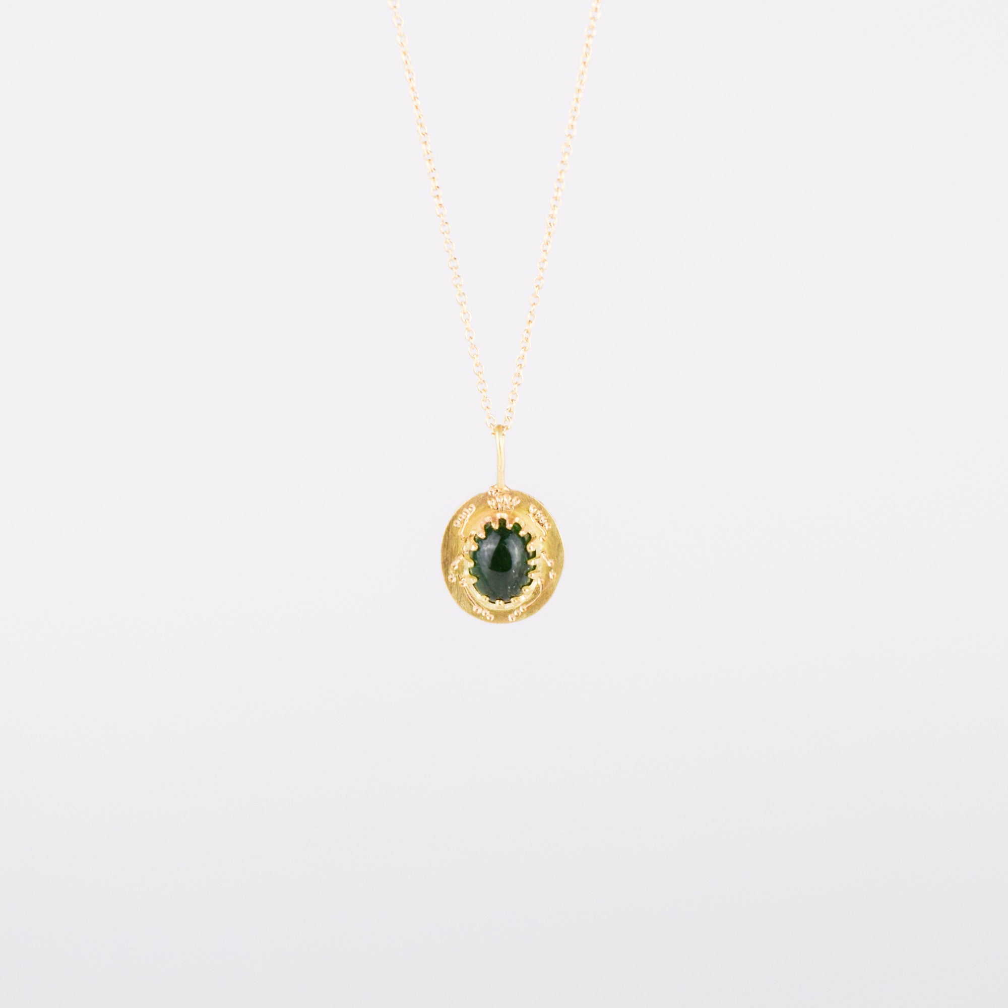 Gold necklace with a green gemstone pendant on a light gray background