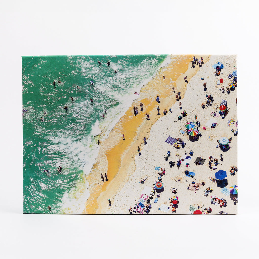Jigsaw puzzle with beach scene with people and umbrellas, green water, and yellow sand.