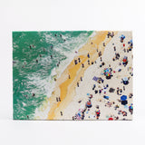 Jigsaw puzzle with beach scene with people and umbrellas, green water, and yellow sand.