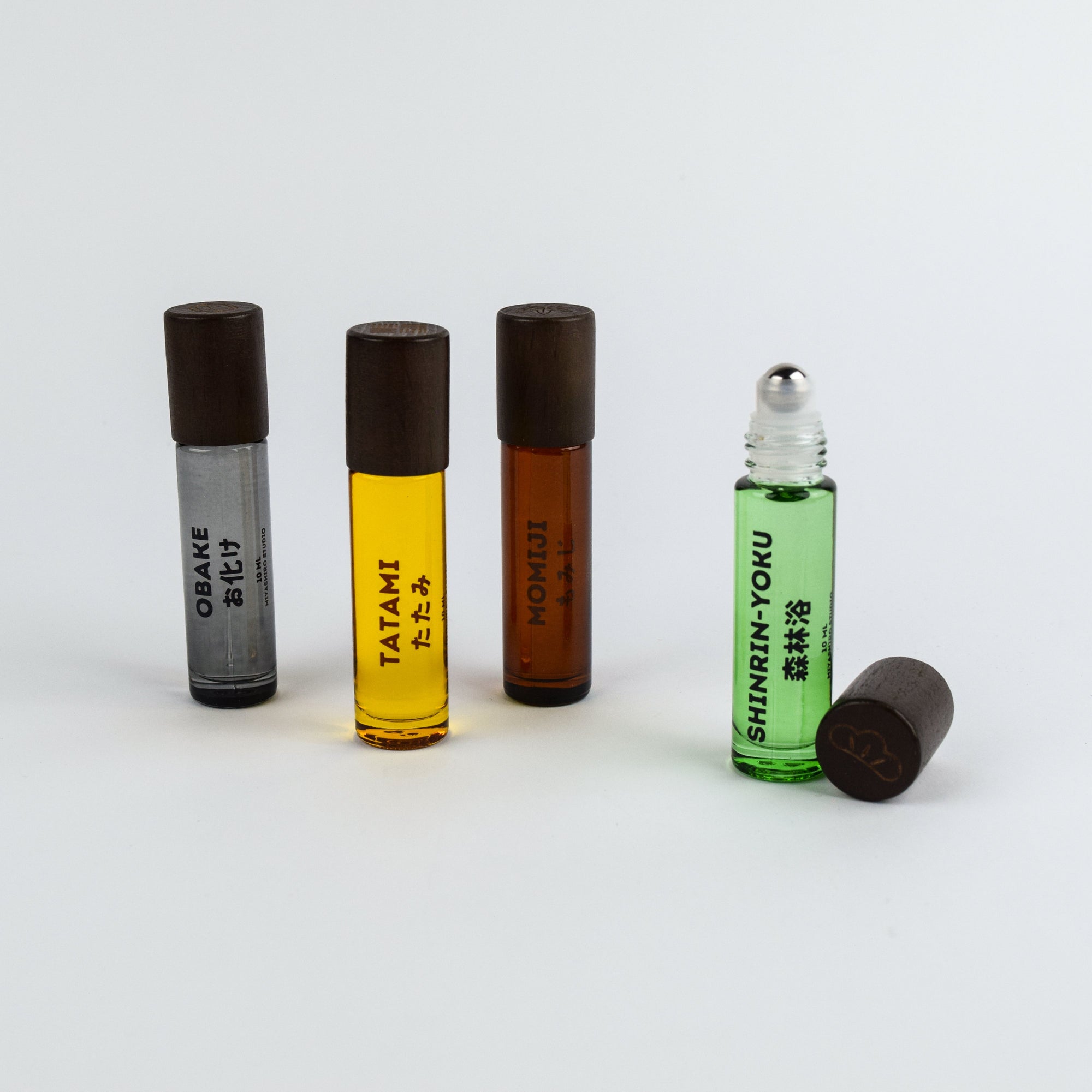 Four roller bottles with different colored liquids and black caps on a white background