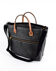 Gray waxed canvas  tote bag with tan leather handles and accents on a white background
