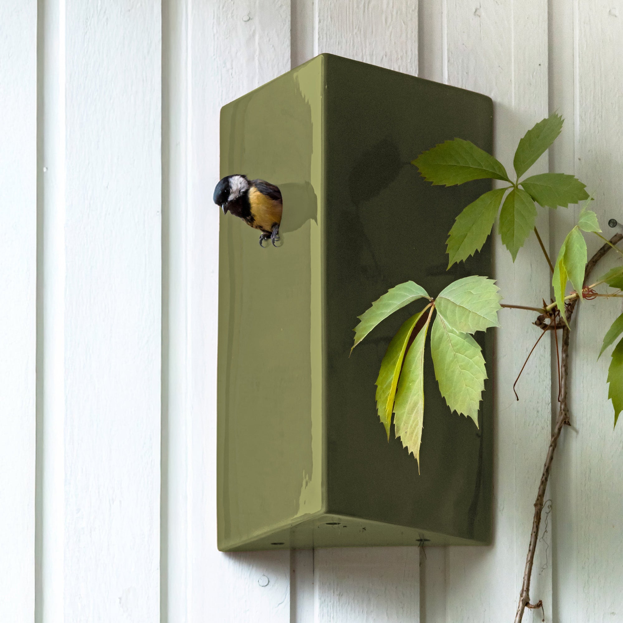 Green birdhouse on a white wooden wall with a bird perched on top