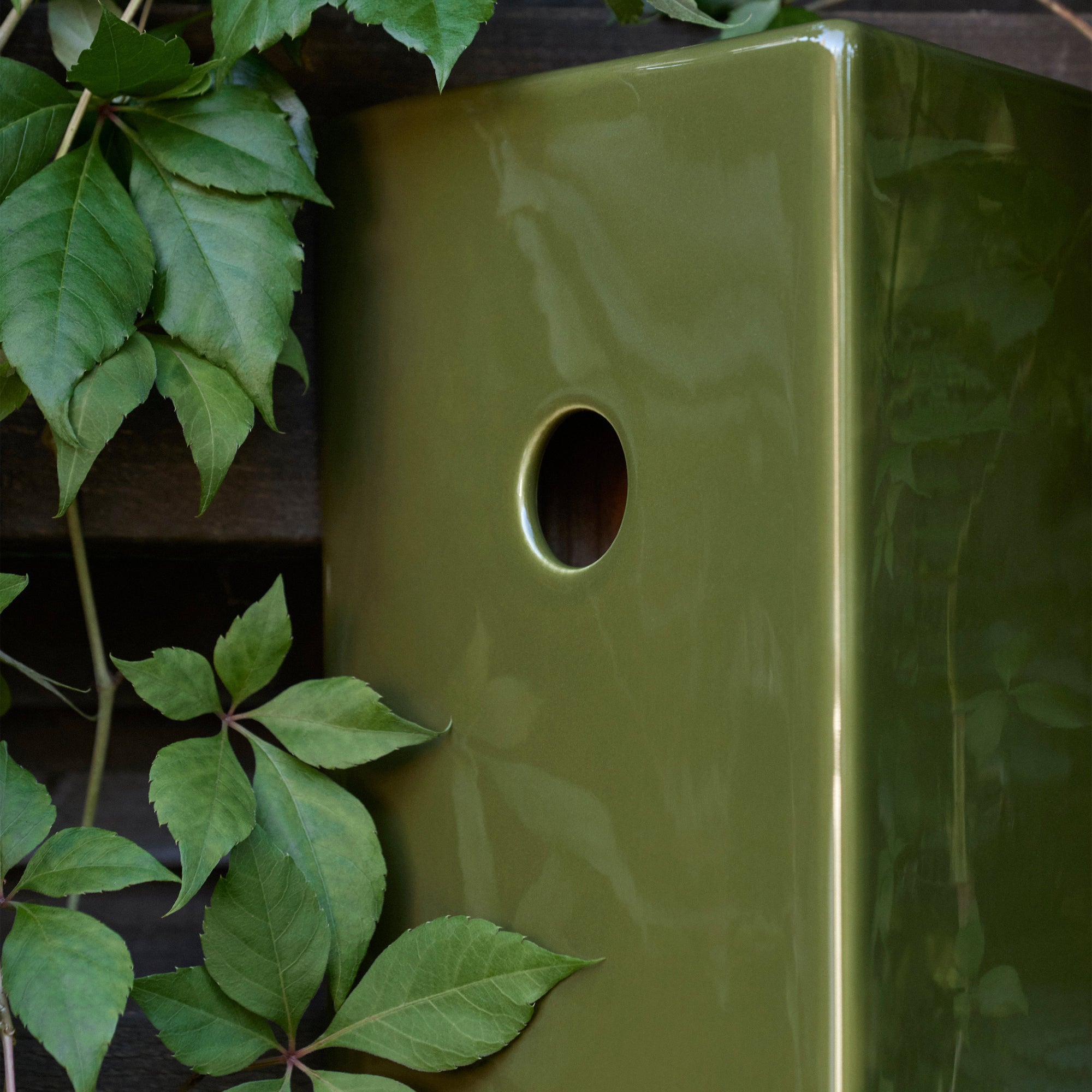 Green ceramic bird house entry detail on a dark background with green leaves.