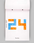 A minimalist white calendar page showing the number 24 in blue and orange with small white dots, labeled January 2021 and Sunday, photographed against a light gray background.