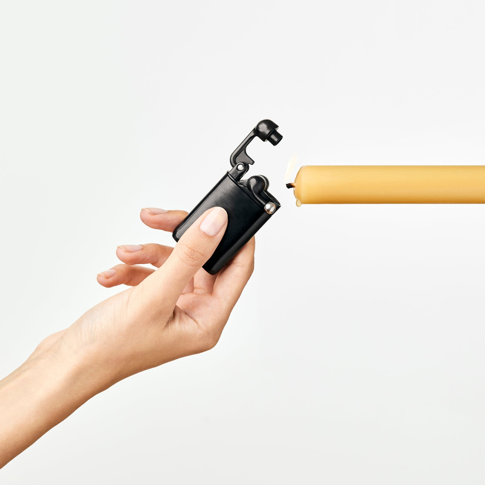Hand holding a black lighter with a yellow candle on a white background