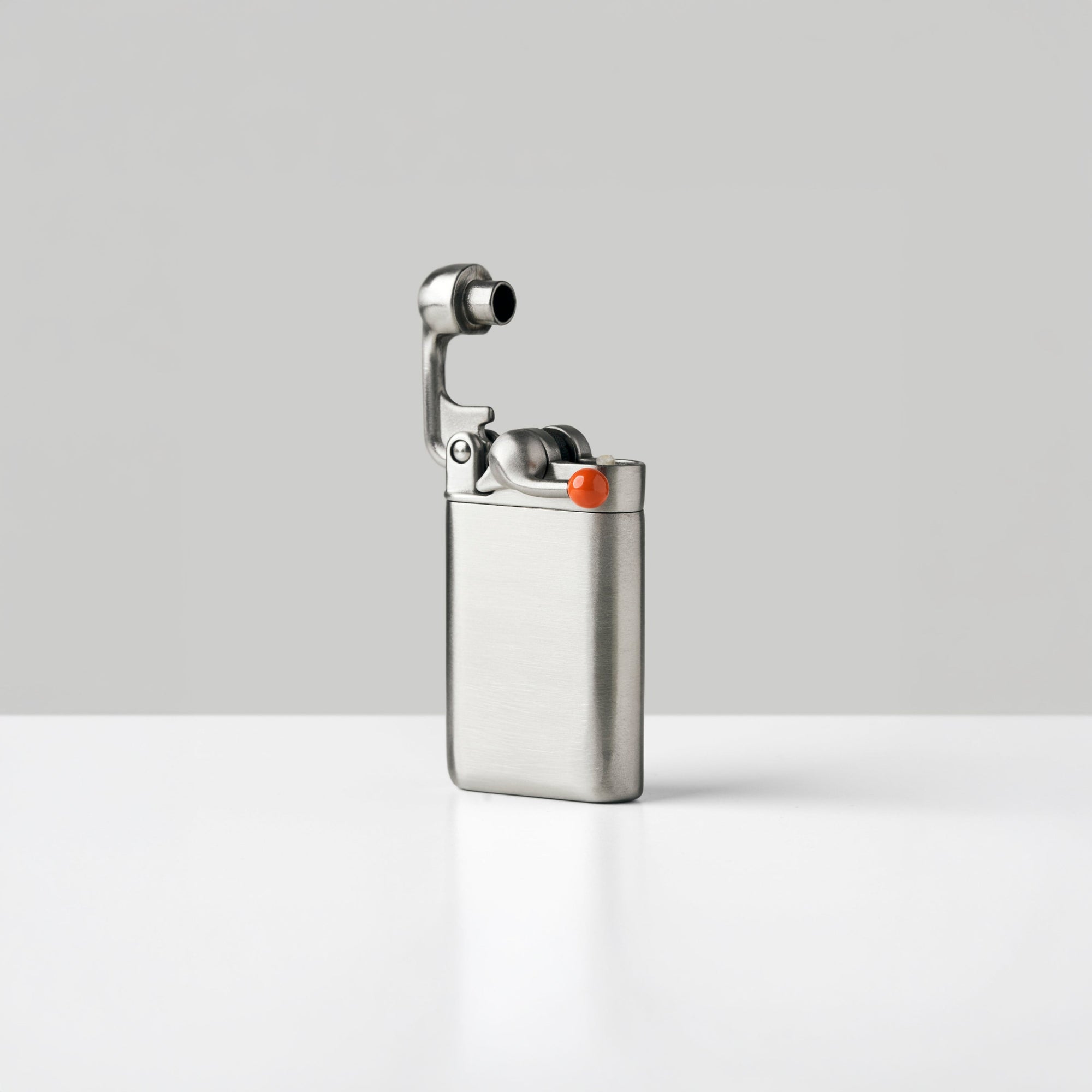 A brushed stainless steel lighter with a small orange tipped swing arm, standing upright on a white surface against a light gray background.